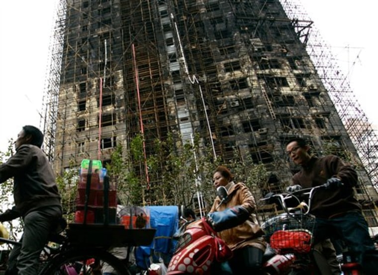 Chinese motorists pass by an apartment building in the background, which was damaged by fire in the downtown area of Shanghai on Monday. Police detained unlicensed welders for accidentally starting a fire that engulfed the high-rise apartment building under renovation in China's business capital that killed at least 53 as public anger grew over the government's handling of the disaster. 